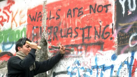 Getty Images Man chipping away at the Berlin Wall, 1989 - with graffiti "Walls are not everlasting"