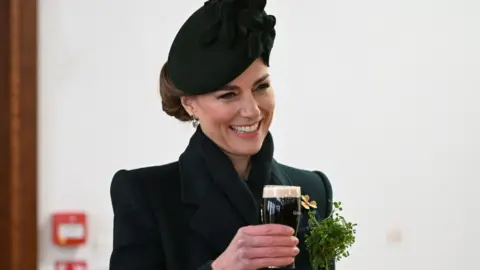 Kate, wearing a green outfit, holding a half pint of Guinness