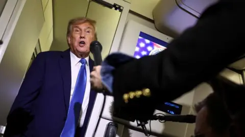 US President Donald Trump is asked questions by reporters on board Air Force One