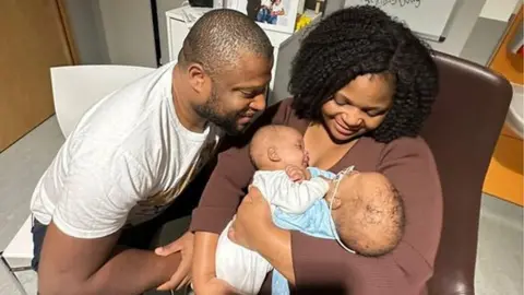 Family photo Dad Christian looks at twins being held by Mum Primrose