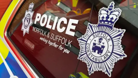 A close-up image of a police car window. Decals depicting the words POLICE Norfolk & Suffolk - working together for you are displayed in between the emblem of each police force.