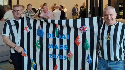 Neil Mitchell Neil (left) holding a Dubai Mags flag