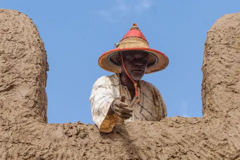 HAMEYE CAPII / AFP / GETTY IMAGES A man gestures for more building materials from a rooftop.
