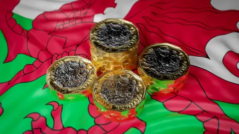 Four small piles of pound coins on top of a very slightly crumpled Welsh flag