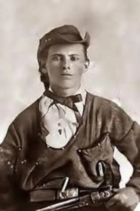 Getty Images Depicted in his youth, a stern looking Jesse James is wearing a cowboy hat, with a pistol resting in his lap. 