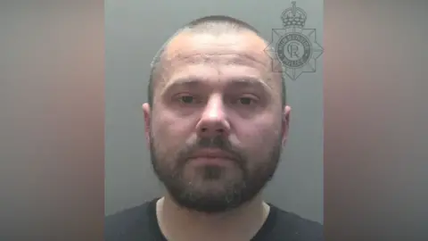Police custody photograph of Radoslaw Golec. He has short dark hair and beard and is wearing a black shirt.