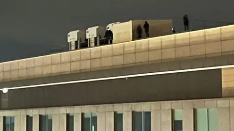 MICH2255 Between four and six blurry dark figures can be seen on the rooftop.