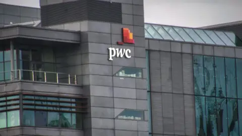 Getty Images Outside PWC building. It is a dark grey building with white writing of "PWC".