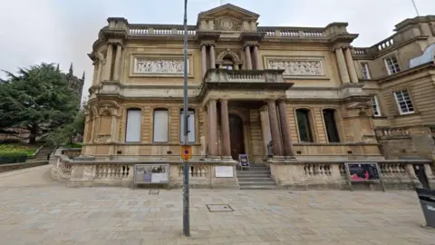 Wolverhampton Art Gallery, a two-storey building, with columns at the entrance. St Peter's Gardens are visible on the far left of the image.