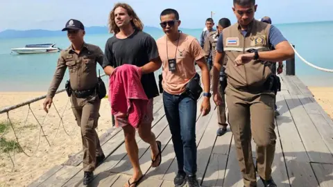 Getty Images Daniel Sancho Bronchalo (2nd L) being escorted by Thai police during a reenactment of his alleged homicide in August 2023