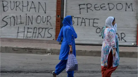 AFP Women walk past a shuttered shop with pro-militant slogans spray painted on