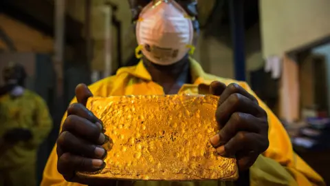 A mine worker in a different country displays a large ingot of gold.