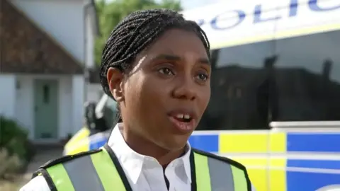 Kemi Badenoch wearing white shirt and yellow vest during interview