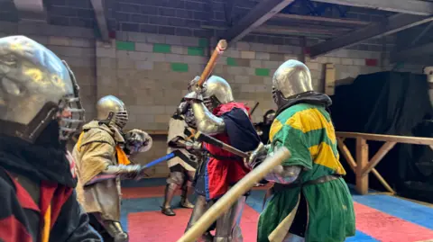 BBC Three men in armour and colourful tunics fight with wooden sticks