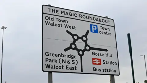 Local Democracy Reporting Service Directional sign of Swindon's Magic Roundabout showing the routes to the town centre, the Old Town Walcot West, Greenbridge Park and Gorse Hill railway station