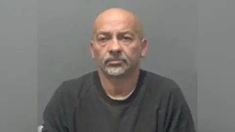 Bedfordshire Police A police mugshot of John Angeli, who is bald with a grey goatee. He is wearing a grey top.