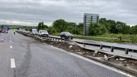 A damaged central reservation with cars driving slowly along one side while the other is completely closed. 
