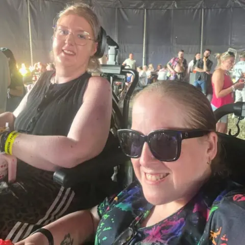 Supplied Amy Atherton and Mary Rawlinson in wheelchairs with glasses with a crowd behind them.