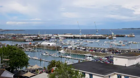 Guernsey's St Peter Port harbour. It shows boats on the water, cranes and car parking facilities. 