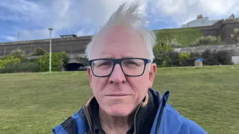 A man with black frame glasses and white hair.