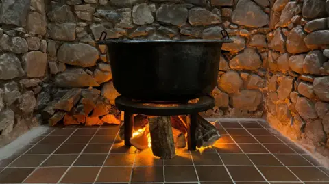 A cast iron post resting above burning wood on a tile floor surrounded by stone wall. 