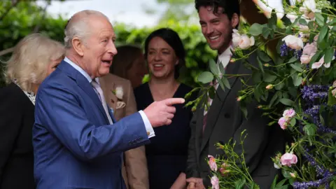 PA King Charles III points at a flower as Queen Camilla looks on during their visit to The RHS and The King's Foundation Curious Garde