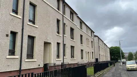 Street view of pebble-dash flats behind a black iron fence