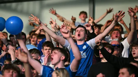 PA Media Fans shouting on a football terrace, some with arms aloft.