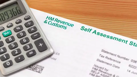 A calculator and a tax self assessment form sitting on a wooden desk