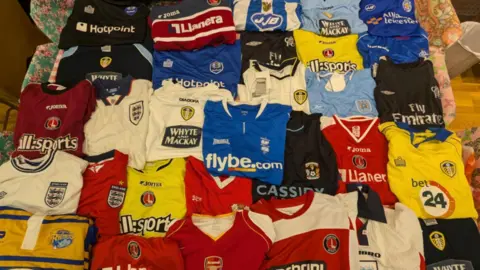 About 30 football shirts, of various bright colours, can be seen laid out and folded in rows inside.