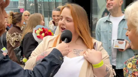 A woman with red hair shows off a tattoo on her chest with the lyrics of Jane McDonald.