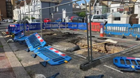 Hsin-Yi Lo/BBC Two sinkholes on a residential road. There are metal fencing and barricades around them.