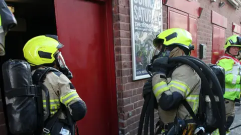 South Yorkshire Fire and Rescue Service Two firefighters wearing protective equipment stand outside an entrance door to the Leadmill.