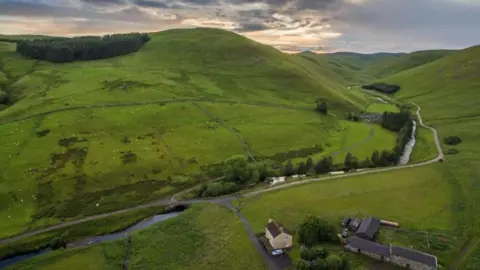 Ian Glendinning An aerial view of the Coquet Valley in the Cheviot Hills with a river cutting through deep green rolling hills and a farm at the base of the image 