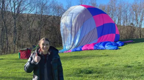 Alicia Hempleman-Adams standing in a field in front of a deflating hot air ship with her thumb up and smiling