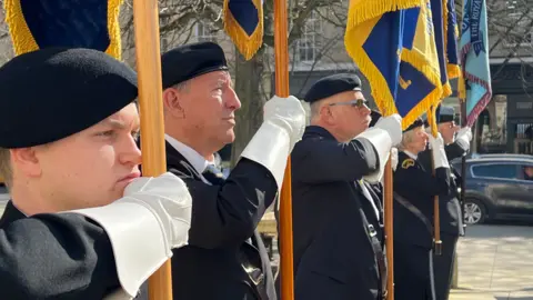 Four men and a woman stand with military flags in their uniform in Cheltenham town centre on a sunny day