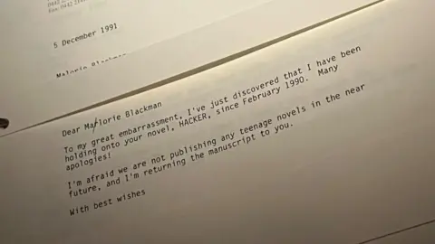 Andrew Turner/BBC Picture of a letter dated 5 December 1991, which reads: 
Dear Marlorie (with a crossed out 'r') Blackman
To my great embarrassment, I've just discovered that I may have been holding onto your novel, HACKER, since February 1990. Many apologies! I'm afraid we are not publisihing any teenage novels in the near future, and I'm returning the manuscript to you. With best wishes.