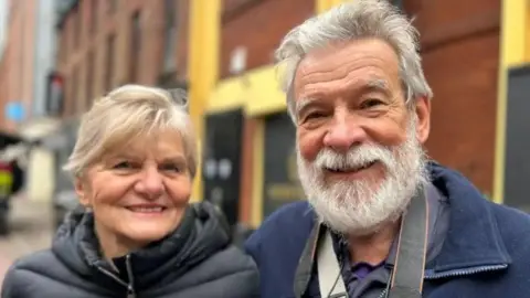 Passengers John and Monica in Belfast. Both are wearing navy coats.