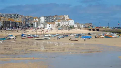 St Ives harbour on a cloudy but sunny day. Lots of boats are on the sand during low tide.