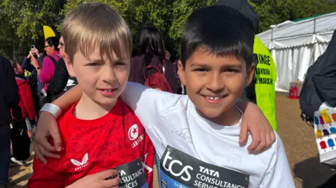 Two young boys stand with their arms over each others shoulders.