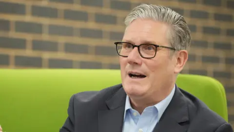 AP Sir Keir Starmer, wearing glasses and sitting on a green sofa. 
