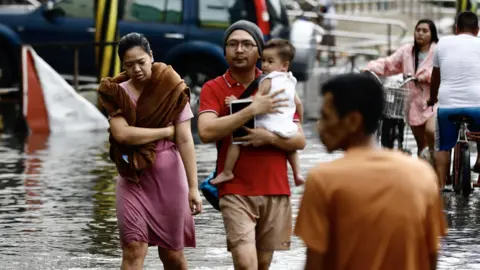  EPA-EFE/REX/Shutterstock Pedestrians wade through the water on a flooded road in the Philippines.