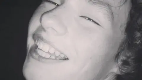 A black-and-white photograph of a smiling Gabriel Santer, who has dark curly hair.