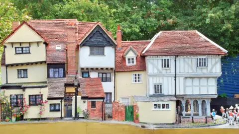 Simon Evans A model of a medieval row of buildings. The buildings have three storeys and have windows in random spots throughout. Some models of small people have been created to stand outside part of the building. 