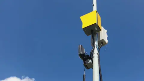 A yellow box with two sensors, attached to a lamppost.