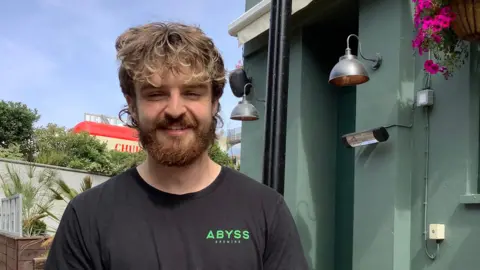 Laura Raymond / BBC A man wearing a black t-shirt with green writing on it, reading "Abyss".