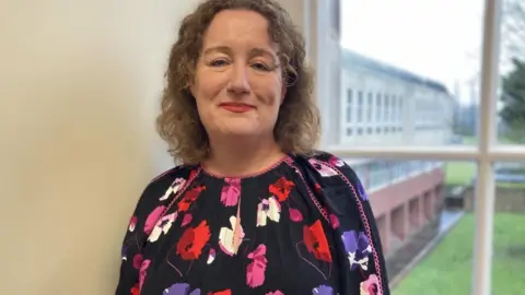 BBC/Michelle Lyons Louise Wallace, director of public health North Yorkshire, pictured wearing a floral dress and standing in front of a window through which can be seen grass and a modern office building