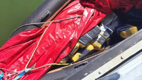National Crime Agency Drugs divided and wrapped as blocks hidden beneath a red tarpaulin in an black inflatable boat.
