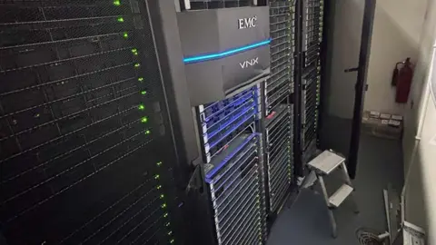 City of London Police A row of computer servers, tall stacked black computer cabinets with multiple trays and flashing green lights