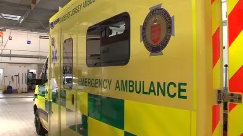 BBC The side of a Jersey ambulance. It is mainly yellow with some green and text reading States of Jersey Ambulance and Emergency Ambulance.